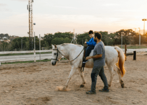 A boy with a disability riding a horse with a teacher during equine therapy